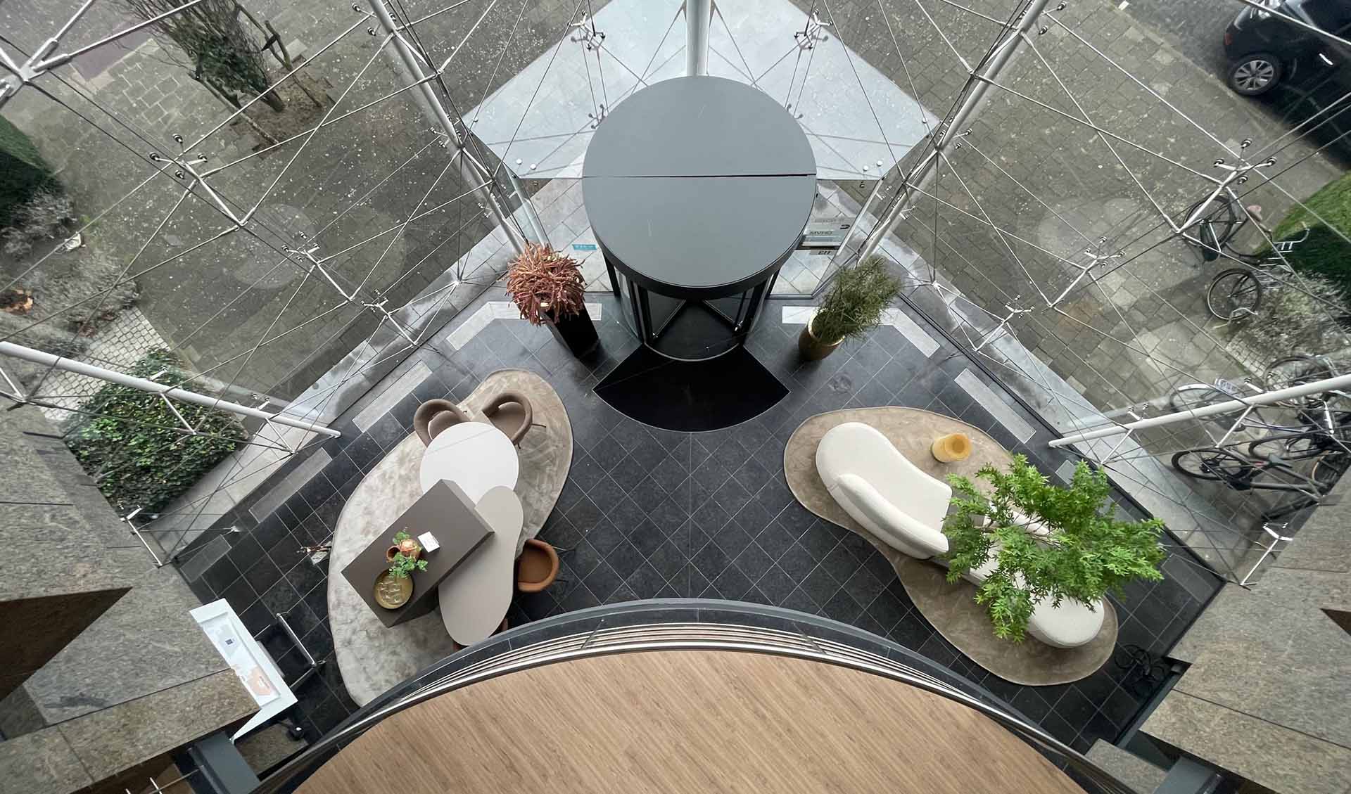 Home – Marcel Lebesque Concepts Bovenaanzicht van het gerenoveerde atrium met ronde zitbanken, koffiebar en groen rond de centrale lift — kantoorgebouw Eindhoven